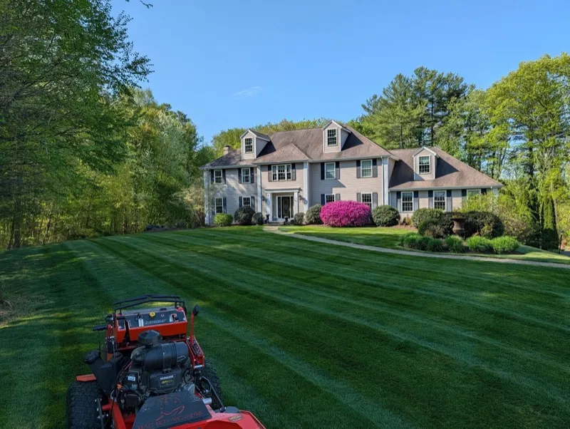 Freshly striped front lawn in front of a colonial home, with a White's mower in the foreground
